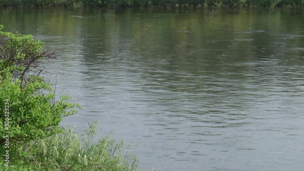 The sun is reflected in the clear water of the river. Bushes and grass are in the foreground. The sun is reflected in the clear water of the river. Bushes and grass are in the foreground.