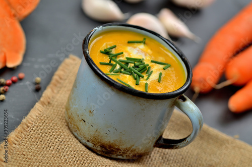 Pumpkin soup with cream and fresh chive in old enamel cup.