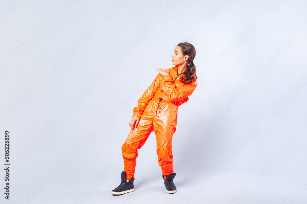Full length image of talented teenage girl with brunette hair wearing bright orange jumpsuit dancing, showing hip hop move, youth hobby activities. indoor studio shot isolated on white background Full length image of talented teenage girl with brunette hair wearing bright orange jumpsuit dancing, showing hip hop move, youth hobby activities. indoor studio shot isolated on white background