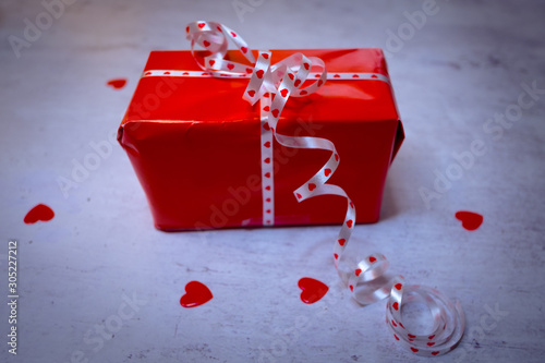 Christmas box in red paper wrap and white bow surrounded by red heart confetti.