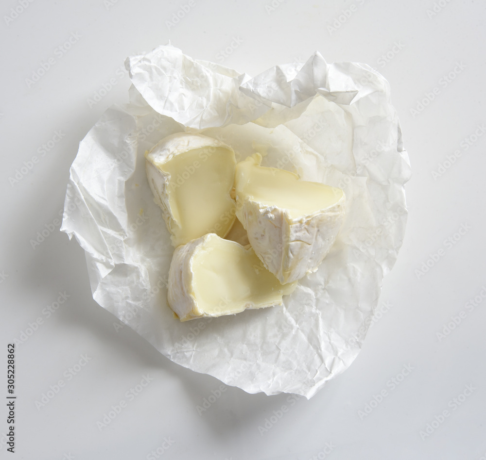 Brie cheese on paper in box on white background Brie cheese on paper in box on white background