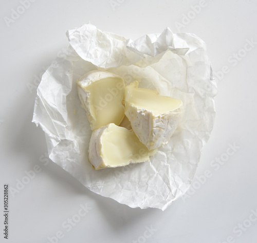 Brie cheese on paper in box on white background