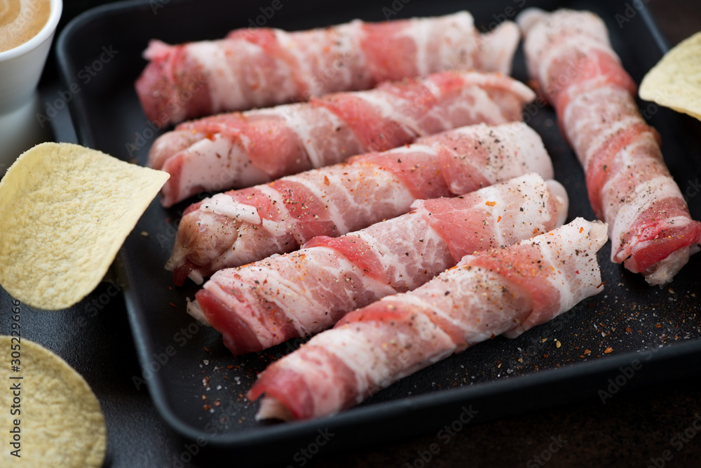 Close-up of raw fresh sausages wrapped around with bacon, selective focus, studio shot