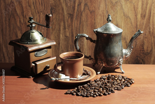 Coffee still life. A cup of coffee, a coffee grinder, a coffee pot and spilled coffee grains on a background of wood texture.