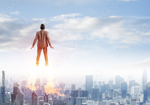 Businessman in suit and aviator hat flying in sky