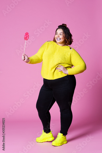 Obraz na plátně Cheerful plus size model in casual clothes with big lollipop, fat woman in black