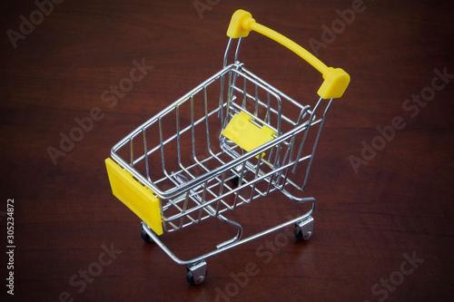 Yellow shopping cart or trolley on wooden background close up