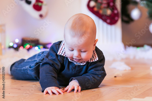 Little boy on floor with fireplace and Christmas presents on background