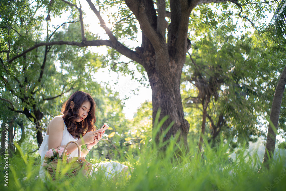 Beautiful asian women sitting in green tree park using smartphone Beautiful asian women sitting in green tree park using smartphone