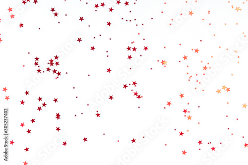 Red stars glitter confetti on white background. Festive backdrop.