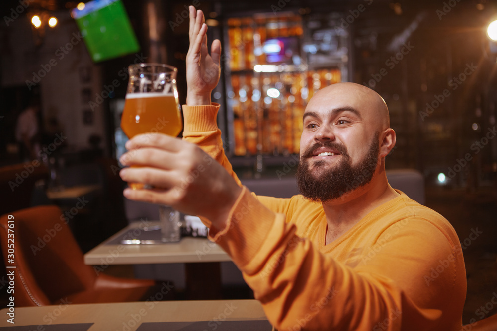 Excited bearded man praising his beer. Happy man looking with love at the beer glass he is holding