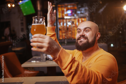 Excited bearded man praising his beer. Happy man looking with love at the beer glass he is holding