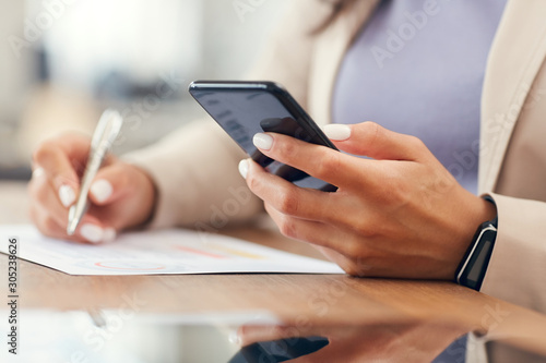 Close up of successful businesswoman holding smartphone while working at desk in office, copy space