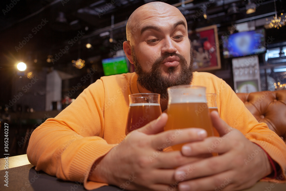 Funny bearded man blowing kisses towards his beer glasses, copy space. Alcohol love, craft beer concept