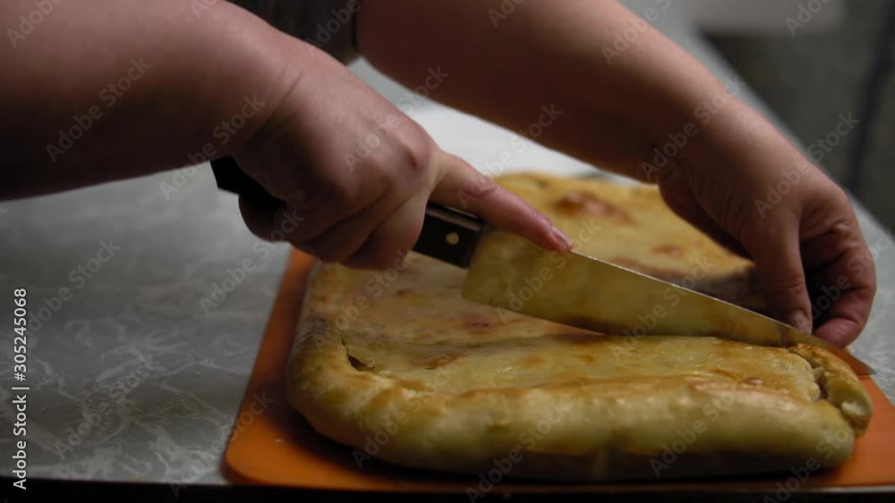 Close-up of a woman's hands with a knife cutting a homemade hot potato pie into pieces on a wooden Board in the kitchen. Close-up of a woman's hands with a knife cutting a homemade hot potato pie into pieces on a wooden Board in the kitchen.