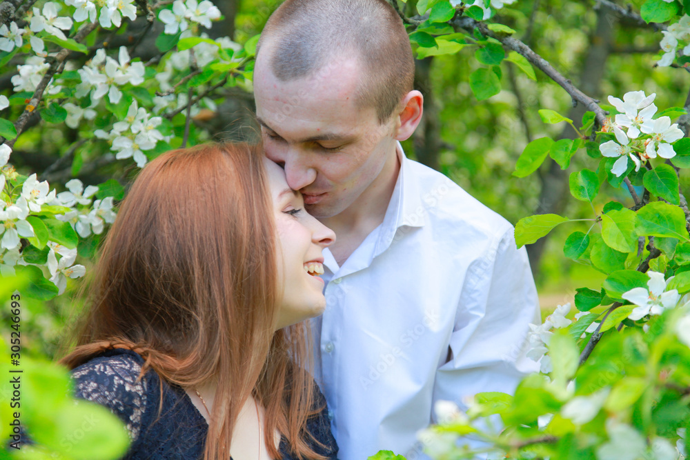 Young couple in fruit orchard apple garden with blossom branches walking together and have a date