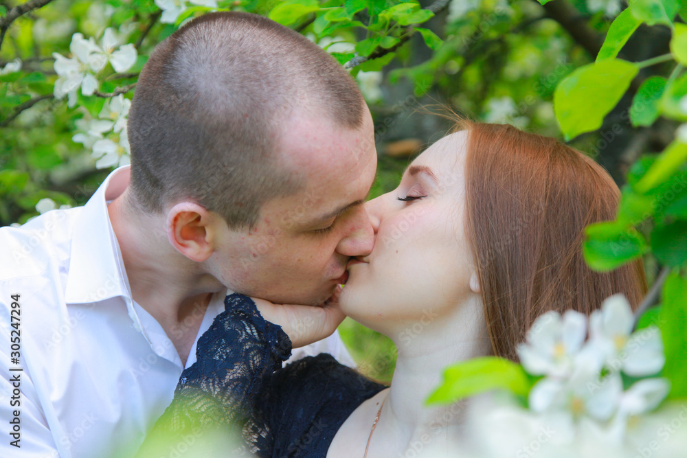 Obraz premium Young couple in fruit orchard apple garden with blossom branches walking together and have a date