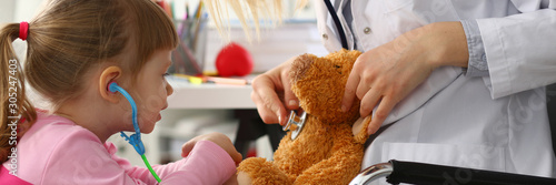 Obraz na płótnie Little girl hold in arms toy stethoscope playing with teddy bear