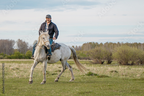 Rider on white horse rides through pasture.