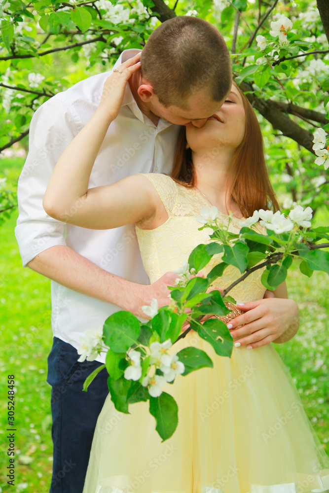 Fototapeta premium The bride and groom are walking in the apple orchard, posing under the branches of an apple-tree.