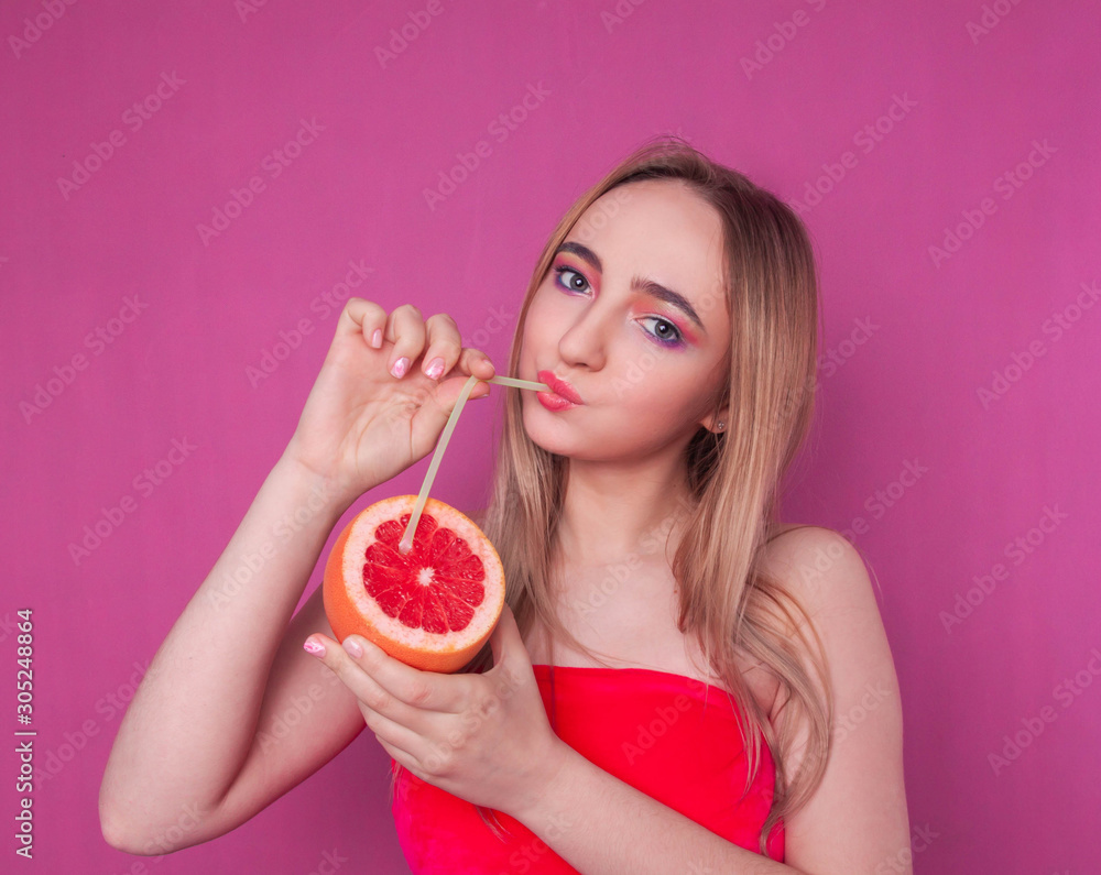 portrait of a beautiful fashionable blonde girl drinking juice from a tube stuck in a grapefruit on a pink background portrait of a beautiful fashionable blonde girl drinking juice from a tube stuck in a grapefruit on a pink background
