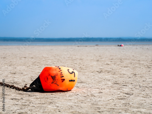 Close up of the orange buoy aying on a dry beach.