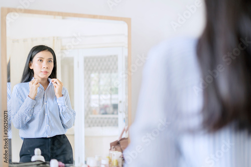 Elegant Asian businesswoman buttoning up shirt in front of mirror getting ready for work