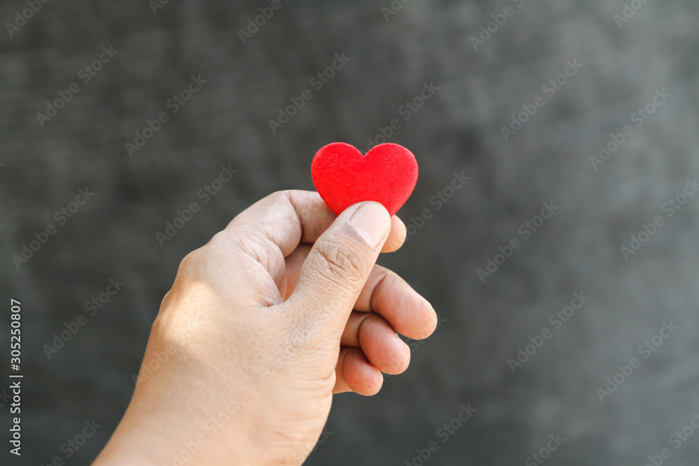 Hand holding single red heart on black background, copy space, Valentine’s day concept.