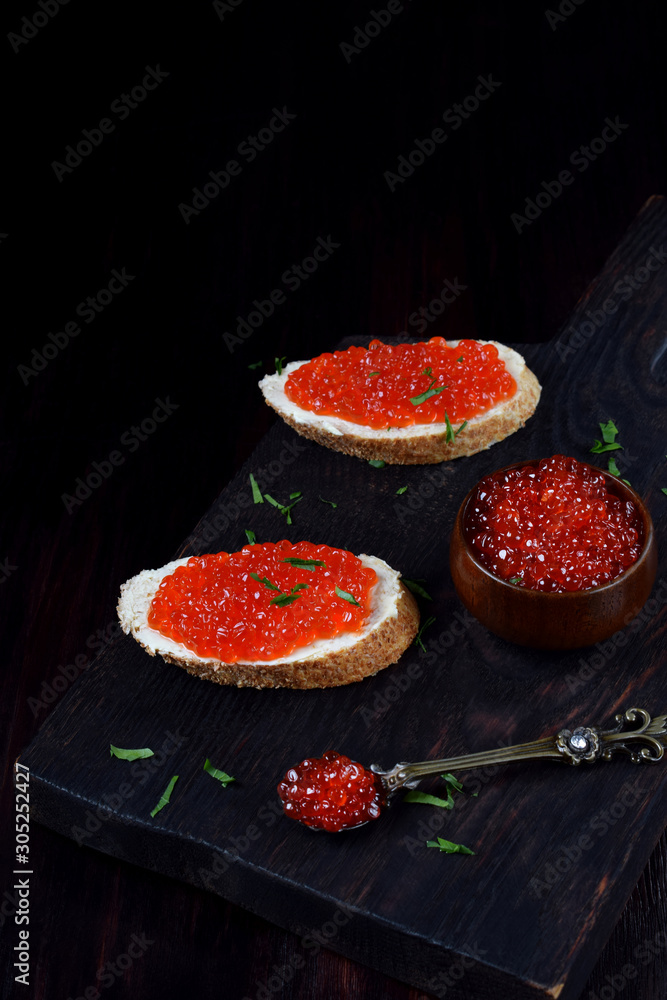 Sandwiches with bran bread, red caviar and butter on black wooden board Sandwiches with bran bread, red caviar and butter on black wooden board