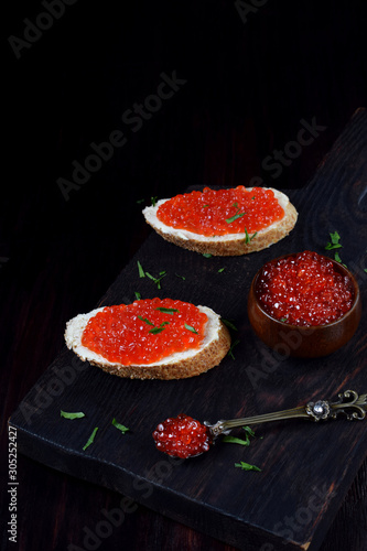 Sandwiches with bran bread, red caviar and butter on black wooden board