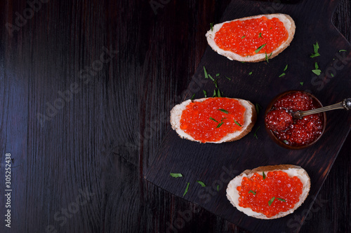 Sandwiches with bran bread, red caviar and butter on black wooden board. Copy space