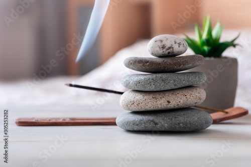 Relax, meditation process at home. Bedroom interior. Pyramid of zen stones, incense stick, flower.
