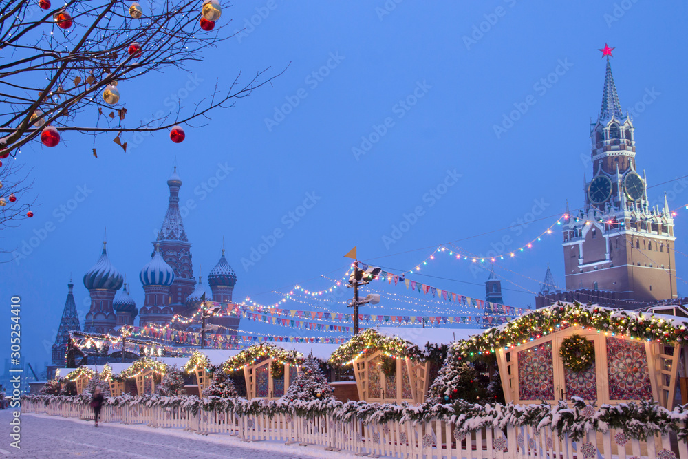 Christmas market and christmas tree next to the GUM store on Red square in Moscow. Christmas ornaments and lights with Saint Basil’s Cathedral and blue sky in the background