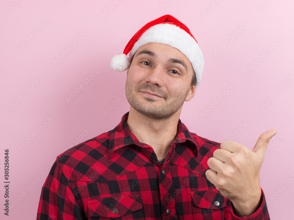 Emotions on the face, smile, joy. A man in a plaid rabbit and a Christmas red hat, on a pink background, copy space. Emotions on the face, smile, joy. A man in a plaid rabbit and a Christmas red hat, on a pink background, copy space.