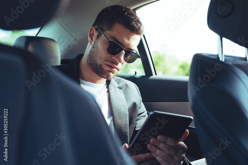Businessman sitting on back seat of car and touching digital tablet © zorandim75