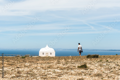 Tourist photographer walking for the view of the Chapel "Capela de Ermida da Memória" in Sesimbra, Portugal/