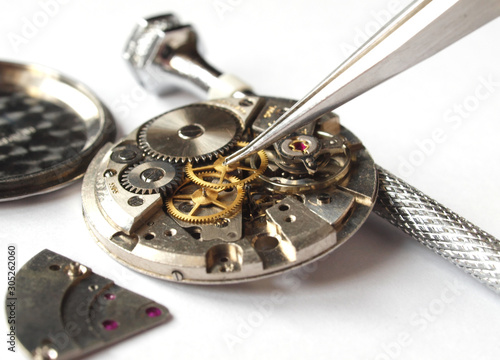 watchmaker working on vintage watch mechanism taking small gear with tweezers