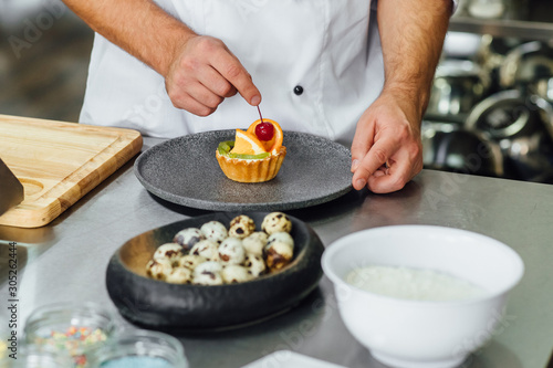 Pastry chef in the kitchen decorating a cake of fruit, candies. Confectioner is decorating cakes cooking class, culinary, bakery, food and people concept.