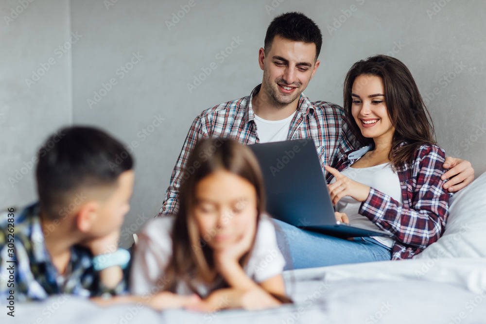Two happy parents, lying at bedroom and using laptop. Weekend time with children. Two happy parents, lying at bedroom and using laptop. Weekend time with children.