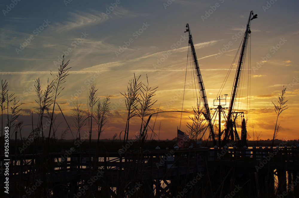 A docked shrimp boat with see oats in foreground and sunset in background.  On the river in Darien, GA.