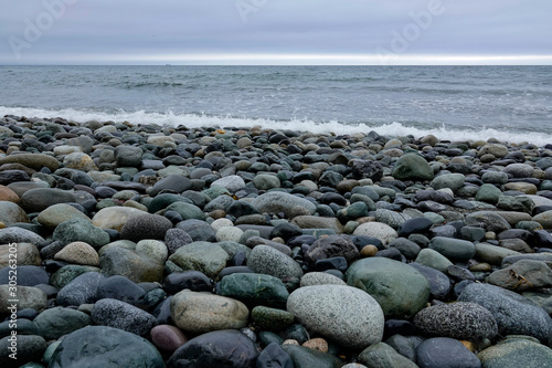 This rocky beach on Puget Sound is very difficult to walk on. The tide is out revealing the smooth and beautifully colored stones. Low angle with level horizon at top third. It is a cloudy day.