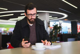 Businessman or manager sitting at a public place with a tablet and pile of documents. Telecommuting, working during a cofeebreak downtown concept: young male person with documents and a tablet