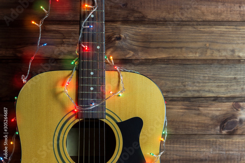 Acoustic guitar in a New Year's garland, guitar in a garland under a wooden wall, copy spaсe