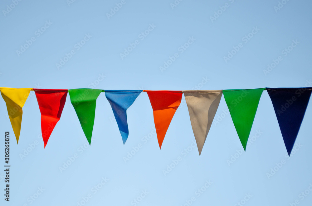 A line of holiday flags hanging on a background of blue sky. Festival flags in the park. The city is getting ready for the celebration. A line of holiday flags hanging on a background of blue sky. Festival flags in the park. The city is getting ready for the celebration.
