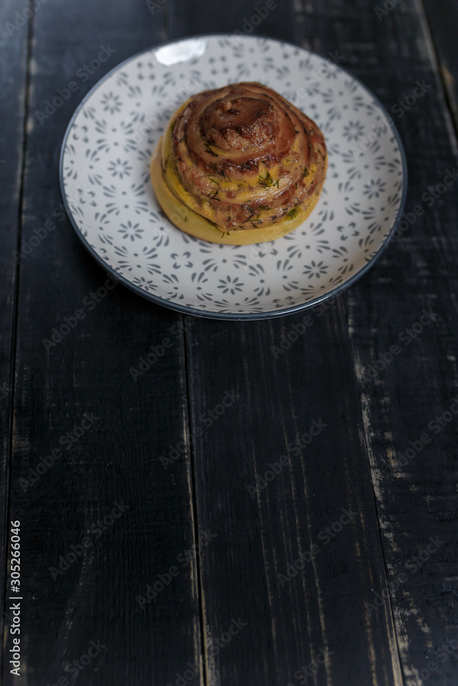 Vertical shot of cheese and dill bread bun on plate standing on black wooden background. Tasty unhealthy food. Diet, nutrition, eating habits concept. Place for text. Vertical shot of cheese and dill bread bun on plate standing on black wooden background. Tasty unhealthy food. Diet, nutrition, eating habits concept. Place for text.