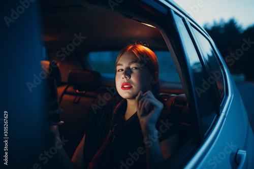 Young woman sitting back seat inside car vehicle at night. Taxi call concept.
