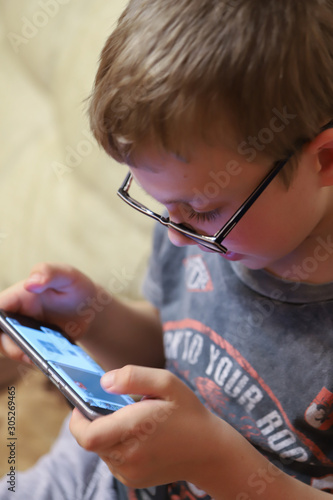 blond boy with glasses playing video games on the phone, dependence on the game 