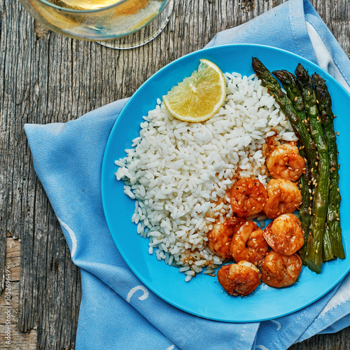 Shrimps and asparagus stir fry with rice on a blue plate with sesame seeds. Delicious seafood meal. Top view, directly above shot.