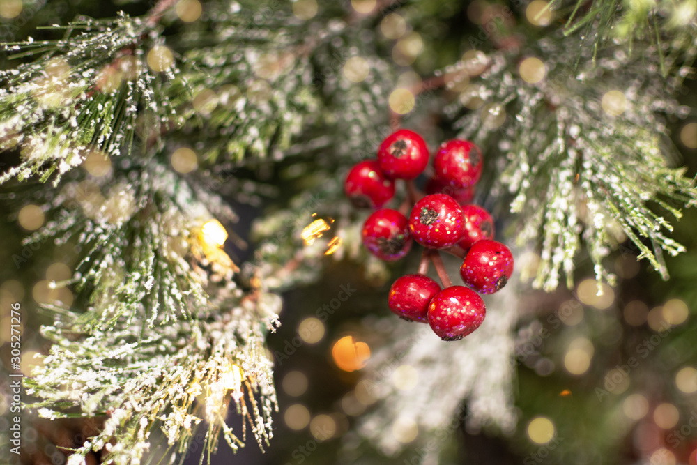 Christmas evergreen tree decorated with red holly berries, bright garland bokeh and artificial snow.