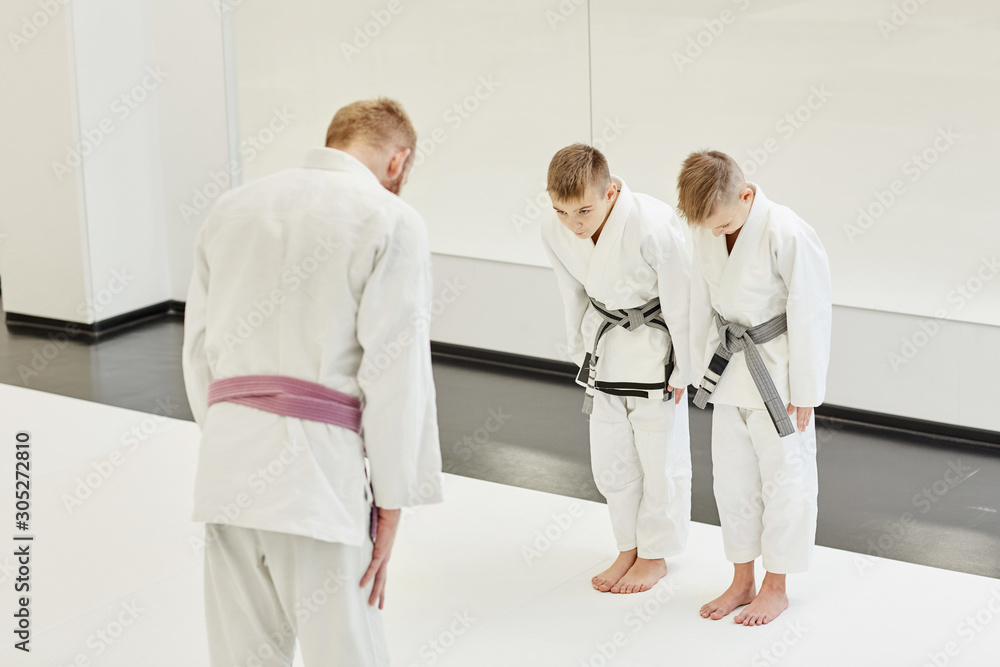 Coach in kimono tanding and greeting his students before lesson in the gym Coach in kimono tanding and greeting his students before lesson in the gym